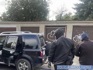 Policjanci w ubraniach cywilnych, w tle samochód marki Land Rover koloru czarnego