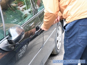 Zdjęcie poglądowe mężczyzny stojącego przy aucie na parkingu i próbującego dostać się do wnętrza bez użycia kluczyków.