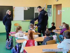 Prowadzący w szkolnej klasie pogadankę z dziećmi umundurowani policjanci.
