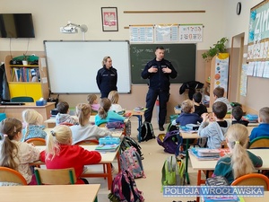 Prowadzący w szkolnej klasie pogadankę z dziećmi umundurowani policjanci.