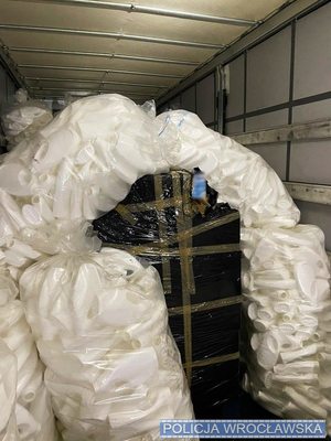 Wnętrze naczepy ciężarowej ze stojącym na podłodze ładunkiem w postaci toreb z pustymi opakowaniami plastikowymi oraz pudłami na paletach owiniętych czarną folią.