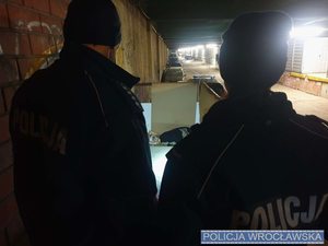 Dwoje umundurowanych policjantów sprawdzający miejsca przebywania osób w kryzysie bezdomności.