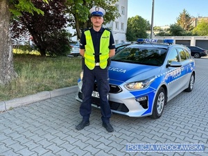 Umundurowany policjant ruchu drogowego stojący przy oznakowanym radiowozie.