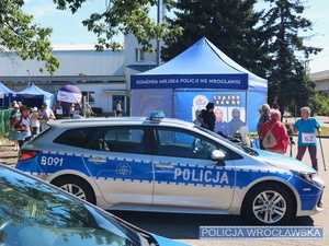 Stojące na parkingu przy Hali Orbita oznakowany radiowóz Policji oraz punkt informacyjno-promocyjny służby w Policji.