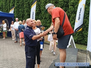 Komendant Miejski Policji we Wrocławiu mł. insp. Rafał Siczek wręczający puchar stojącemu na podium jednemu z uczestników czwartej edycji Mistrzostw Senioralnych o Puchar Komendanta Miejskiego Policji.