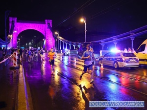 Funkcjonariusze ruchu drogowego nadzorujący oznakowanym radiowozem ruch na jednym z  wrocławskich mostów w trakcie zabezpieczenia 10 edycji Nocnego Półmaratonu we Wrocławiu.