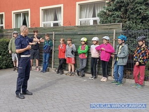 Policjant ruchu drogowego stojący przed grupą nastolatków w trakcie omawiania zasad bezpieczeństwa w ruchu drogowym przed przystąpienia do części praktycznej egzaminu na kartę rowerową.