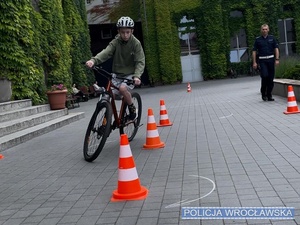 Dzieci pod nadzorem policjanta w trakcie przejazdu torem przeszkód w trakcie praktycznej części egzaminu na kartę rowerową.