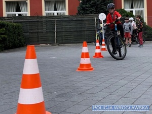 Dzieci pod nadzorem policjanta w trakcie przejazdu torem przeszkód w trakcie praktycznej części egzaminu na kartę rowerową.