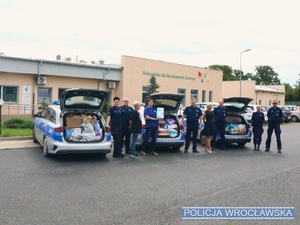 Stojący na parkingu przed radiowozami zaparkowanymi przed wrocławskim Schroniskiem dla zwierząt policjanci i pracowniczka cywilna Policji oraz pracownicy schroniska