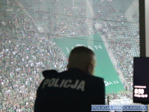 umundurowany policjant koordynujący działania, w tle kibice na stadionie