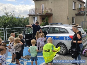 Umundurowany policjant wraz z dziećmi na parkingu przy oznakowanym radiowozie