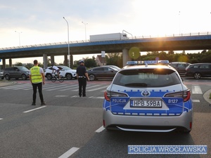 Stojący obok oznakowanego radiowozu, nadzorujący ruch w sąsiedztwie stadionu umundurowany policjant ruchu drogowego