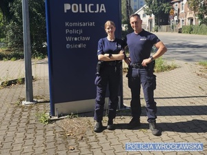 Zdjęcie dwójki umundurowanych policjantów stojących przy banerze z napisem Komisariat Policji Wrocław Osiedle