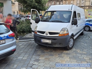 Umundurowani policjanci oraz oznakowane radiowozy stojące wokół busa marki renault na jednej z wrocławskich ulic