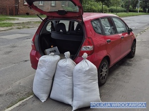 Pojazd osobowy marki Honda stojący z otwartym bagażnikiem przy jednej z wrocławskich ulic, a przy nim trzy worki jutowe wypełnione krajanka tytoniową.