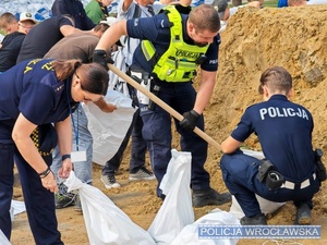 policja pomaga sypać piasek w worki