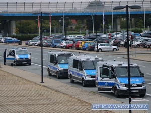 Zdjęcie stojących na parkingu przy stadionie oznakowanych radiowozów typu bus