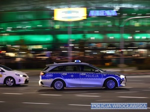 Oznakowany radiowóz przejeżdżający przez skrzyżowanie w sąsiedztwie Miejskiego Stadionu we Wrocławiu.