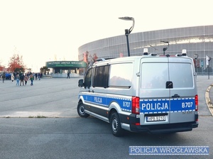 Oznakowany radiowóz policyjny typu bus stojący w okolicy głównego wejścia na stadiom miejski we Wrocławiu.