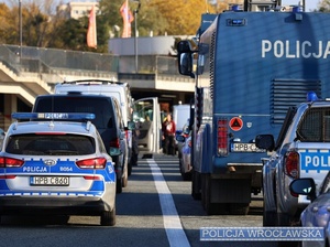 Stojące przed stadionem oznakowane radiowozy oraz pojazdy specjalistyczne Policji.