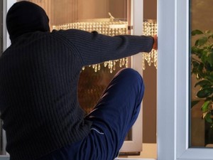 Zdjęcie ilustracyjne zamaskowanej osoby wchodzącej do wnętrza lokalu mieszkalnego przez okno