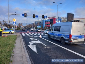 Stojący na jezdni przy jednym z wrocławskich skrzyżowań oznakowany radiowóz policji oraz policjanci i osoby wykonujący swoje czynności w związku ze zdarzeniem drogowym