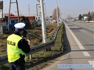 Zdjęcie ilustracyjne funkcjonariusza Wydziału Ruchu Drogowego w trakcie wykonywania pomiaru prędkości na jednej z podwrocławskich dróg.