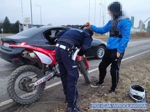 Kontrolujący motocykl na jednej z podwrocławskich dróg policjant ruchu drogowego oraz stojący obok motocyklista.