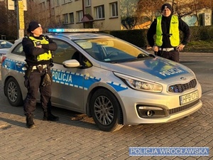 Policjanci Wydziału ruchu Drogowego Komendy Miejskiej Policji we Wrocławiu stojący przy oznakowanym radiowozie zaparkowanym przy jednej z wrocławskich ulic.