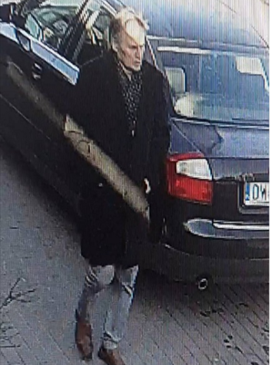 wizerunek mężczyzny w czarnym płaszczu stojącego obok pojazdu