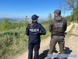 na zdjęciu widać na tle przyrody stojących dwóch umundurowanych funkcjonariuszy policji oraz Straży leśnej