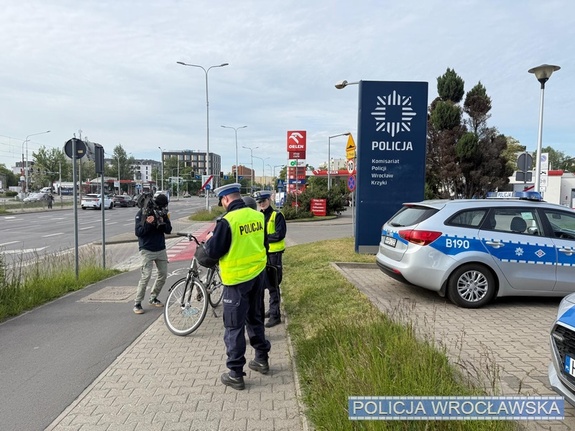 za zdjęciu rowerzystka która kontroluje dwóch policjantów obok operator kamery