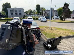 na zdjęciu operator kamery nagrywa policjanta który trzyma w ręku video rejestrator dronu