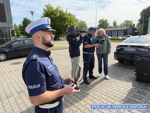 na zdjęciu jest policjant a w tle operator kamery, kobieta i funkcjonariusz policji