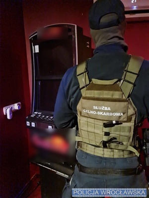 na zdjęciu widać funkcjonariusza tyłem stojącego obok automatu