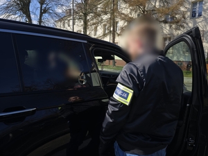 na zdjęciu widać policjanta pionu kryminalnego z naszywką na ramieniu policja stojącego tyłem przy radiowozie nieoznakowanym