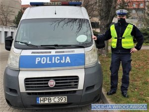 Zdjęcie umundurowanego policjanta stojącego przy oznakowanym radiowozie