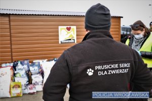 Zdjęcie przedstawiają psy oraz policjantów, którzy wyciągają z radiowozu typu furgon opakowania z karmą dla psów