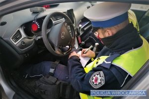 Policjant ruchu drogowego siedzący w radiowozie, podczas sporządzania dokumentacji służbowej