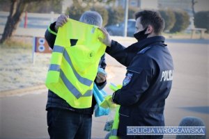 policjant przekazuje odblaskową kamizelkę
