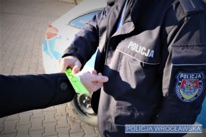 Policjant zakłada odblaskową opaskę na rękaw płaszcza meżczyźnie