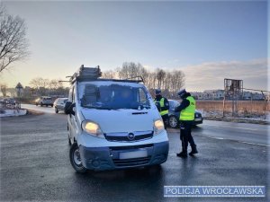 Zdjęcia przedstawiają policjantów kontrolujących pojazdy. Widoczni są funkcjonariusze w granatowych mundurach i żółtych odblaskowych, kamizelkach.