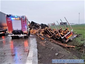 Przewrócony na bok pojazd ciężarowy przewożący drewno oraz wóz straży pożarnej