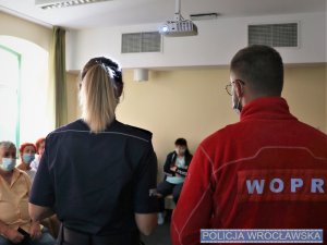 Policjantka z ratownikiem WOPR prowadzący prelekcję stojący przed mieszkańcami Ołbina