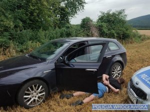 Zatrzymany przez policjantów mężczyzna z kajdankami na rękach leżący obok swojego pojazdu